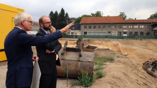 Schulbürgermeister Vorjohann erläutert dem Kultusminister den geplanten Schulneubau. Im Hintergrund das Haus Sieben, das im Frühjahr abgerissen werden soll.