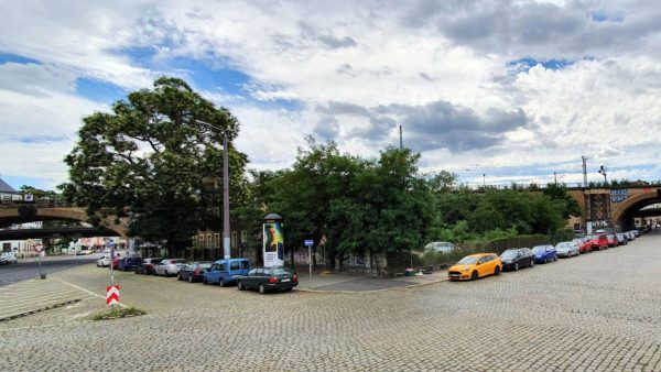 Hinter den Bäumen befindet sich aktuell ein Parkplatz und ein kleines Haus.