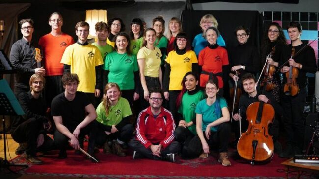 ruppenfoto mit den Sänger*innen des Chors, der Solistin Nina Houshmand (1. Reihe, 3. von rechts) und den Musiker*innen der Musikhochschule sowie Johannes Gerstengarbe (Mitte sitzend), Inhaber des Tonstudios. 