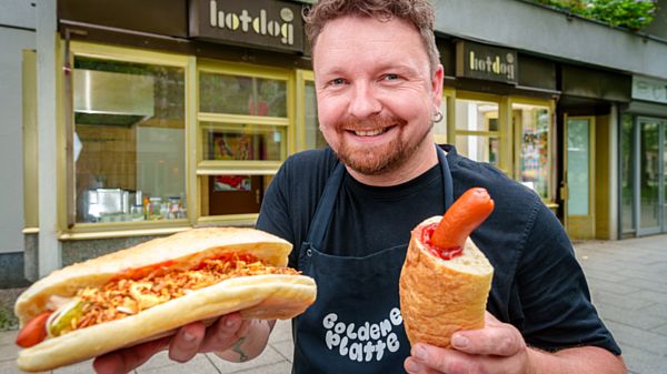 Christian Hagen (40) vom Restaurant Löwe auf der Dresdner Hauptstraße posiert am Freitag (30.06.2023) mit zwei Hotdogs für ein Foto. Der das legendäre Hot-Dog-Stand an der Seite des Löwen soll diese Tage wieder öffnen. Foto: André Wirsig für Vonovia